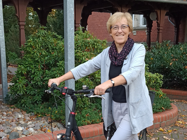 Rita Burmeister stehend mit dem Fahrrad an der Hand, Hospiz- und Palliativdienst, Begleitung sterbender Menschen, Diakonie Hospiz Wannsee, Interview, Berlin-Wannsee