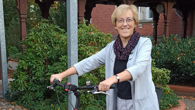 Rita Burmeister stehend mit dem Fahrrad an der Hand, Hospiz- und Palliativdienst, Begleitung sterbender Menschen, Diakonie Hospiz Wannsee, Interview, Berlin-Wannsee